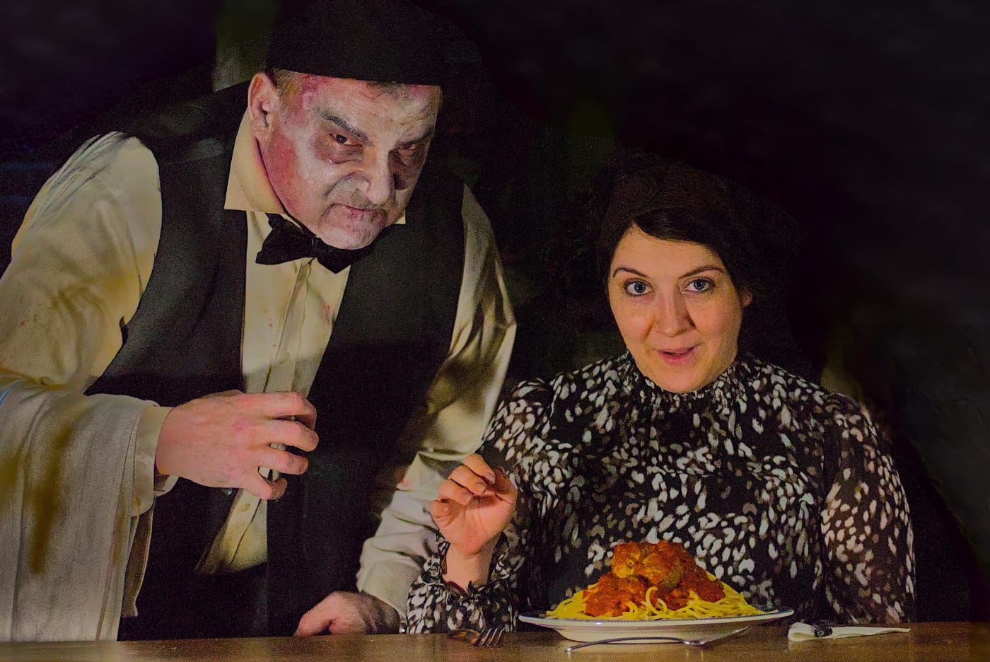 A performer in zombie make-up leans in over a diner mid-meal, a plate of spaghetti and meatballs between them